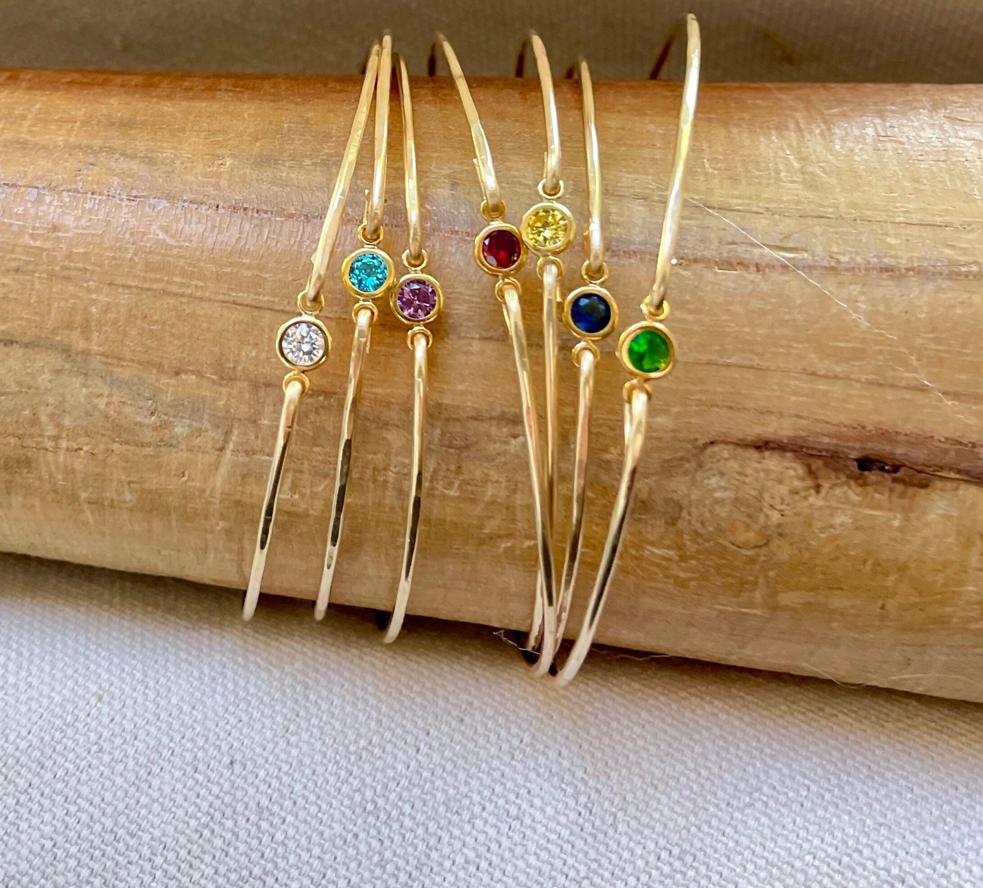Dainty birthstone bangle featuring sparkling CZ diamonds, ideal for stacking and layering, perfect for brides, bridesmaids, and gifts. Bangles displayed on a wooden bracelet display.